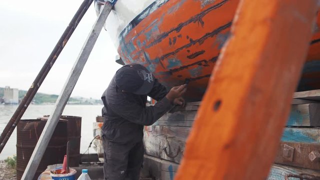 Fisherman Repairs Fishing Boat With Water Proofing Sealant Slow Motion Shot