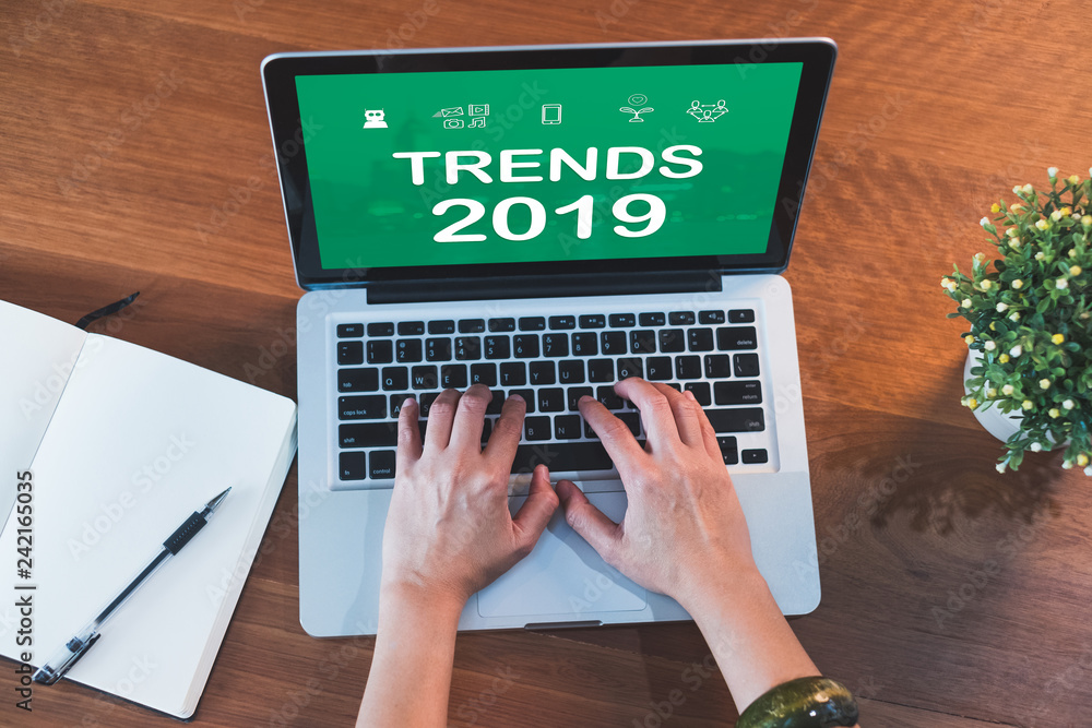 Poster top view hand type trends 2019 on laptop keyboard with open notebook and plant on table at home.working with technology.