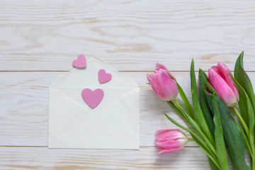 Bouquet  of pink tulips and hearts pattern in paper envelope. Top view, close-up, flat lay on white wooden background