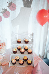Chocolate cupcakes on a white wooden stand. Sweet table and big cake for first birthday