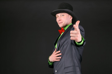Man in a bowler hat is winking and is pointing by his index finger ahead on black background.