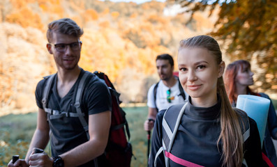 Smiling young hiker woman with backpack trekking in the company of friends