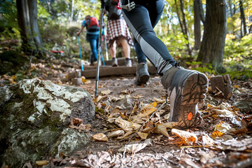 Hiker woman with trekking sticks climbs steep on mountain trail, focus on boot - obrazy, fototapety, plakaty