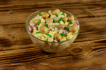 Potato salad with marinated mushrooms, sausage, onion and mayonnaise on wooden table