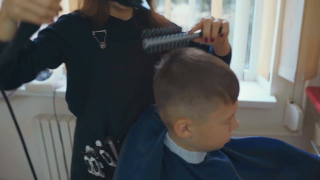 Hairdresser cutting hair with barber scissors in children hairdressing salon.