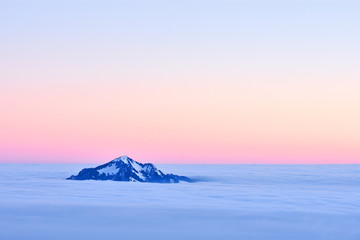 Lonely snow-covered mountain sticking out of a cloud layer (Allgaeu Alps, Bavaria, Germany). Beautiful colorful morning mood just before sunset. Copy space.