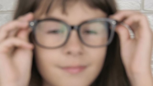 A child with poor eyes wears glasses. Beautiful little girl puts on glasses.