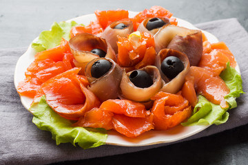 Gourmet restaurant serving a plate of smoked salt, raw white fish fillets and salmon. Delicacy fresh seafood dish with catfish, salmon meat with olives on a plate close-up