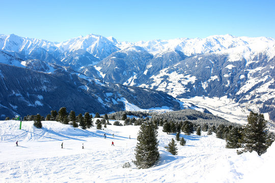 People enjoying skiing on prepared slopes in the Alps on sunny day. Beautiful snowy trees in the mountains. Perfect winter holidays destination for family in modern comfortable Alpine ski resort. © cromary