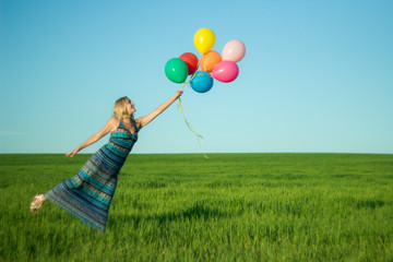 Girl with balloons in the field. Solar and positive energy of nature. Young beautiful woman on the grass in the Park.