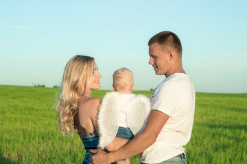 Happy family in a green meadow. A child with angel wings. The concept of family and happiness.
