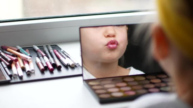 A beautiful little girl at the mirror makes herself a make-up