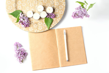 writing materials: a notebook of kraft paper and a pen. beautiful composition of fresh flowers, branches, candles and plates on a white table. Space for text, flat lay, creative layout