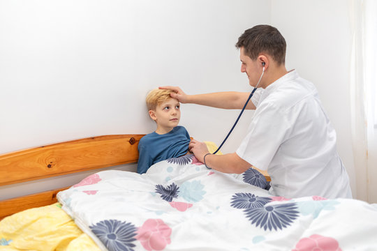 Young Male Doctor Visiting Little Patient At Home To Consult With Stethoscope And Diagnose Him Of Cold Or Fever. Pediatrician Medic And Little Boy During Home Visit. Health And Medicine Concept