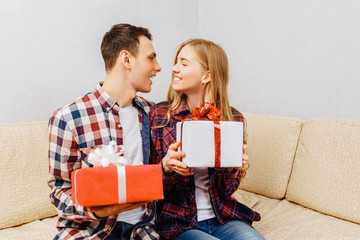young couple, man and woman give each other gifts while sitting at home on the couch, valentines day concept