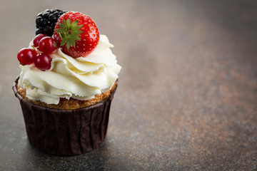 Various sweet berry cupcakes on brown stone background. 