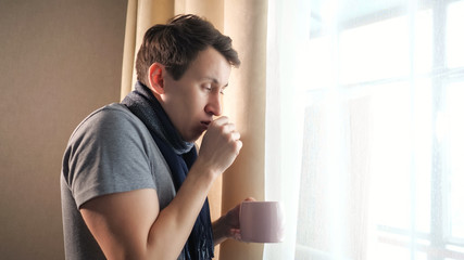Obraz na płótnie Canvas Sick male with mug coughing near window