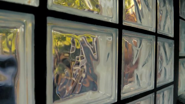 Sun shines through a glass block window in a house. View of the outdoors through the square glass blocks that obscure the view and distort the image on the other side. BOOM UP.