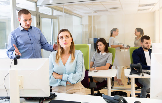 Upset girl sitting at laptop in coworking space while dissatisfied businessman pointing out mistakes in her work