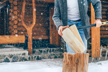 Man chopping wood on snowy yard for a house fireplace with heavy snowflakes background . Winter...