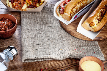 Close up view on traditional american fast food. Hot dog with bacon and cheese on brown background around herbs and spices. Hot dogs, french fries, sause. Copy free space for text logo or brand.