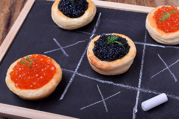Red and black caviar in tartlets on a chalkboard with tic tac toe game