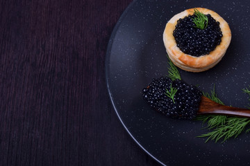 Black caviar in a wooden spoon and puff pastry tartlet on a dark plate © kcuxen