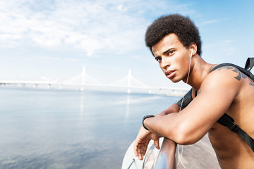 Young sportsman wearing backpack and listening to music while resting after work out