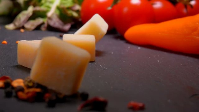 Cubes of Parmesan cheese fall to the black surface of the table on the background of greenery and vegetables