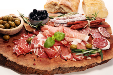 Marble cutting board with prosciutto, bacon, salami and sausages on wooden background. Meat platter