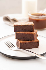 Chocolate brownie square pieces in stack on white plate. American traditional delicious dessert. Copy space.