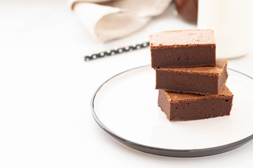 Chocolate brownie square pieces in stack on white plate. American traditional delicious dessert. Copy space.