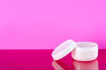 White jar of cream feather on pink background