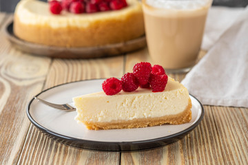 Piece of classic cheesecake with raspberries and coffee on a wooden background. Copy space.