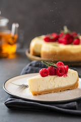Slice of New York Cheesecake with raspberries on a dark background.