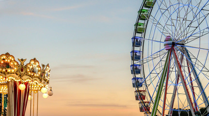 Ferris wheel in a fairground park next to a carousel - obrazy, fototapety, plakaty