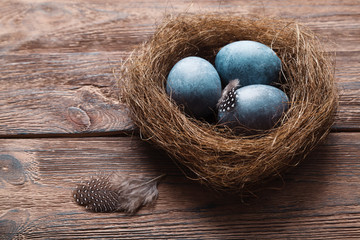 Three marble blue Easter eggs painted by hibiscus, in a nest on a wooden background close-up. The Symbol Of Easter