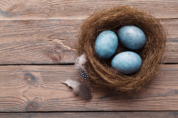 Three marble blue Easter eggs, in a nest with feathers on a wooden background. The Symbol Of Easter. Copy space