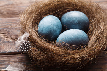 Three marble blue Easter eggs painted by hibiscus, in a nest on a wooden background close-up. The Symbol Of Easter