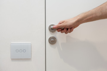 Naklejka premium Light switch next to the door handle. Open white door with metallic handle. The man opens the door