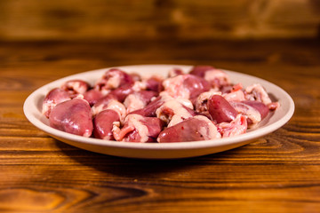 Ceramic plate with raw chicken hearts on wooden table