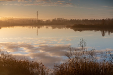 beautiful autumn morning in the countryside near the lake, fog in the distance, beautiful blue sky and cloud reflection in the water