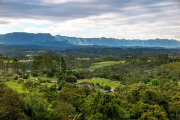 Fototapeta na wymiar Panorama of the region of Lauro Muller, with pastures, forest and mountains of the National Park of Sao Joaquim in the background, cloudy sky, Santa Catarina