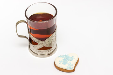 Glass cup with tea in a cup holder on a white background and heart-shaped gingerbread