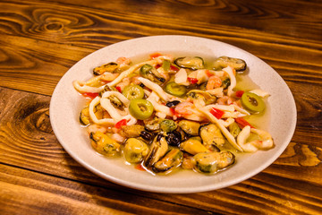 Ceramic plate with different sea food and olives on wooden table