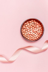 Tan colored glow face pearls blush and pink ribbon on a pastel pink background top view Flat Lay with copy space. Various cosmetic products, Makeup Accessories.