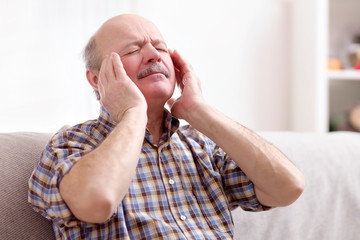 Senior man with mustache having a headache at home