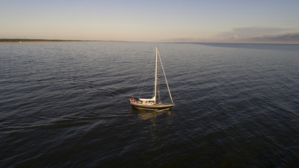 Aerial shot from the middle of the sea of lonely sailboat with coiled sails floats on a calm sea....