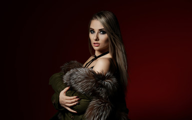 Young sexy fashion woman in fur coat and underwear on dark red