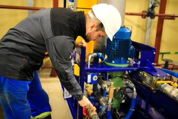Engineer checking oil pump and pressure gauge in industrial plant.